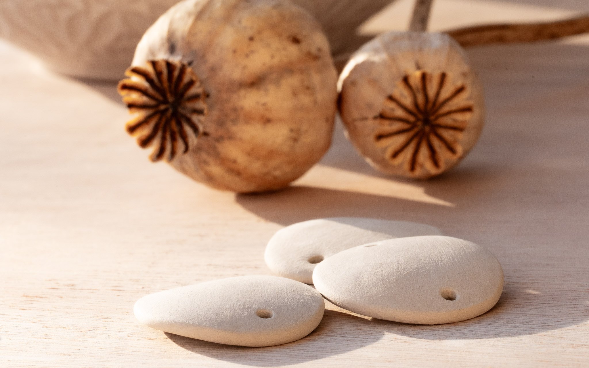 Bracelets en céramique brute en cours de séchage à côté de fleurs de pavot, illustrant l'authenticité de l'artisanat Calagioia.