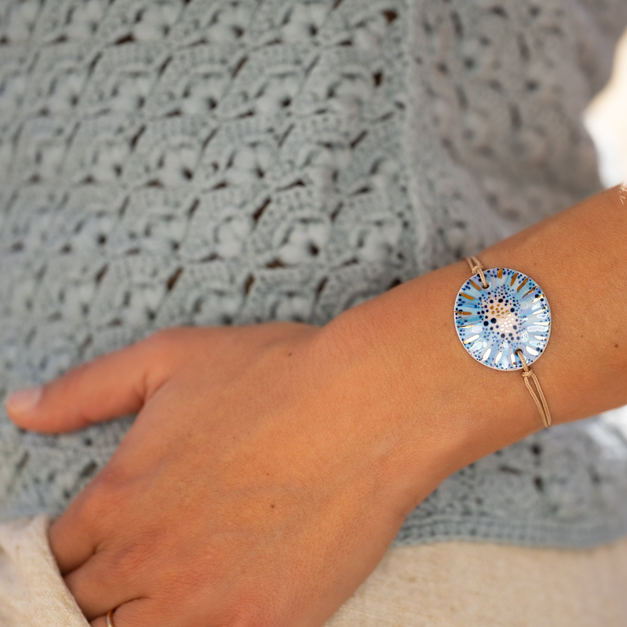 Main dans la poche et tenue estivale en lin, mettant en valeur un bracelet Cala Gioia avec son bijou bleu sur un Lien de Sable.