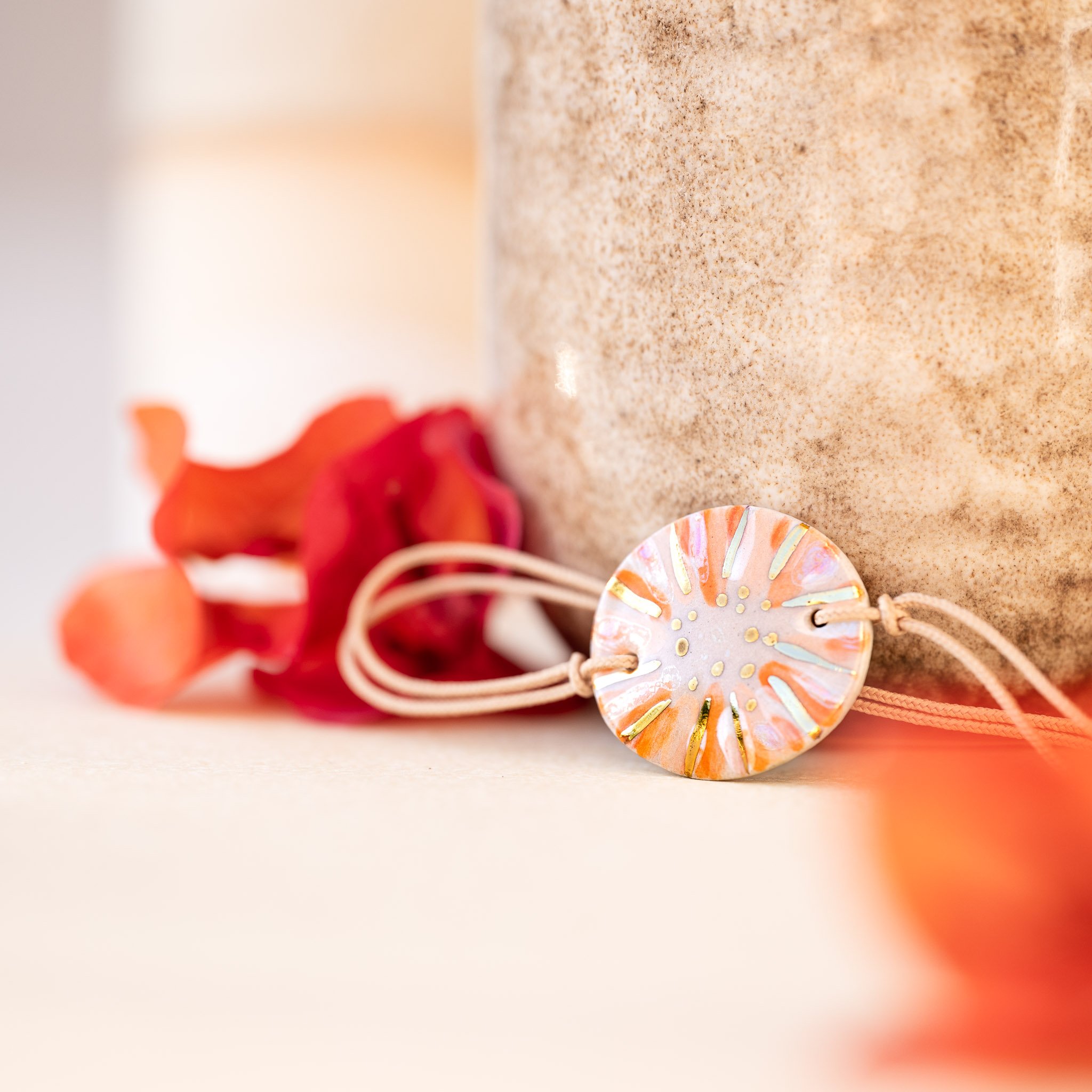 Prendre soin du lien : un bracelet Calagioia aux tons orangés reposant contre un vase artisanal beige, sublimé par la floraison éclatante d'un bougainvillier orange.