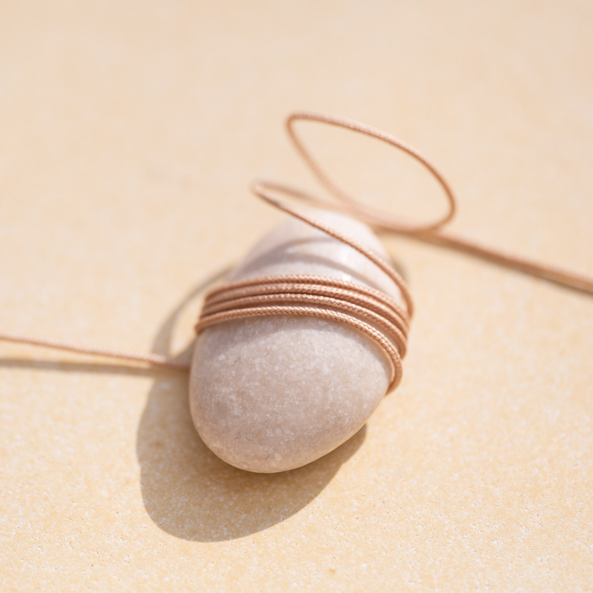 Notre cordon Cala Gioia couleur sable délicatement enroulé autour d'un galet naturel.