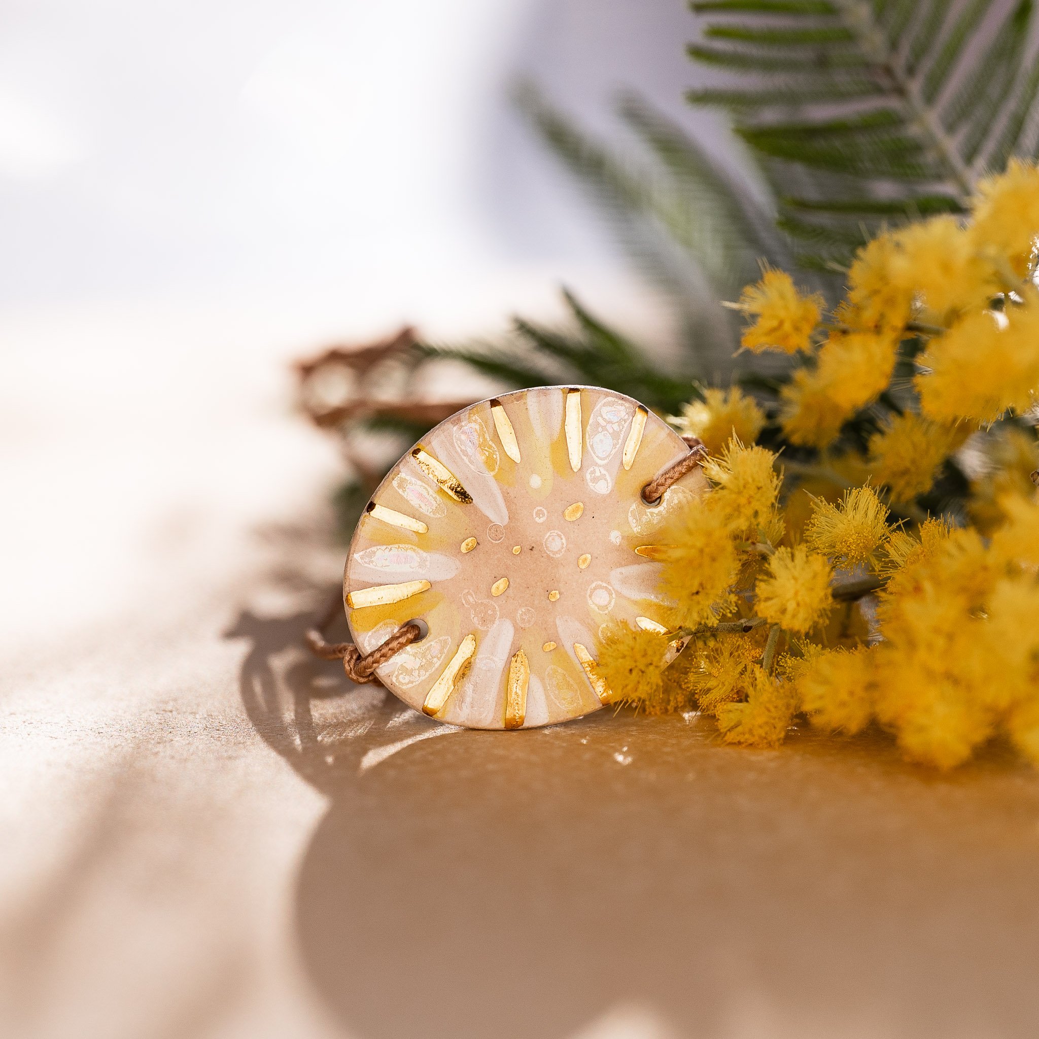Préserver l’éclat de l’or : bracelet jaune Calagioia en harmonie avec une branche de mimosa en fleurs, symbole de la lumière solaire que nous cherchons à capturer et protéger.