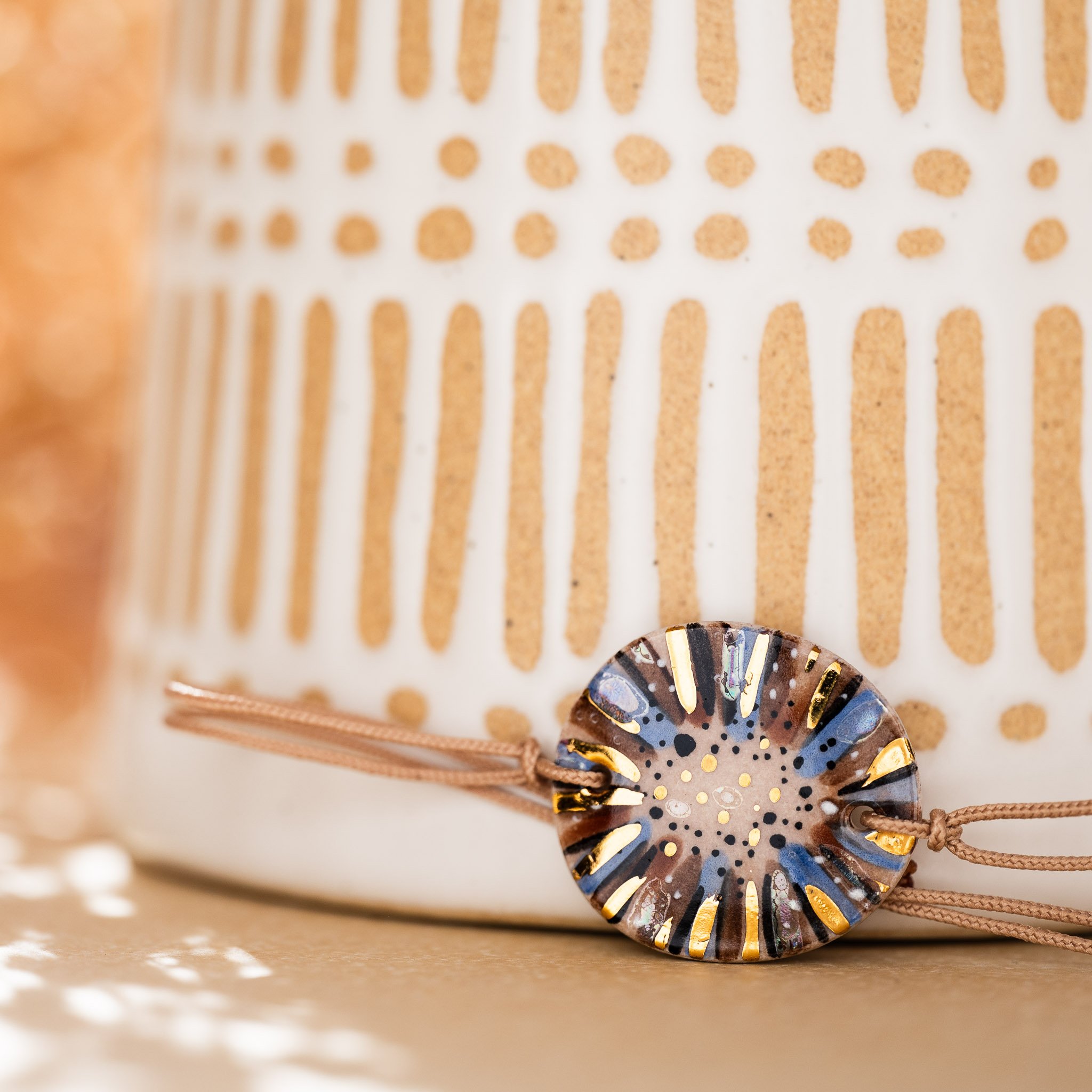 Contraste solaire et minéral : bracelet en or et céramique posé sur une poterie artisanale, illustrant la maîtrise du troisième feu par Calagioia.