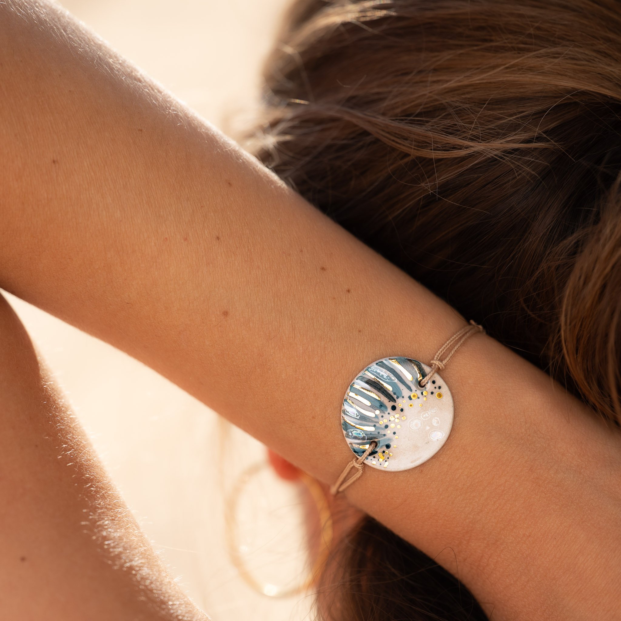 Femme vue de dos passant la main dans ses cheveux, portant un bracelet artisanal CALA GIOIA qui incarne l'authenticité de notre histoire.