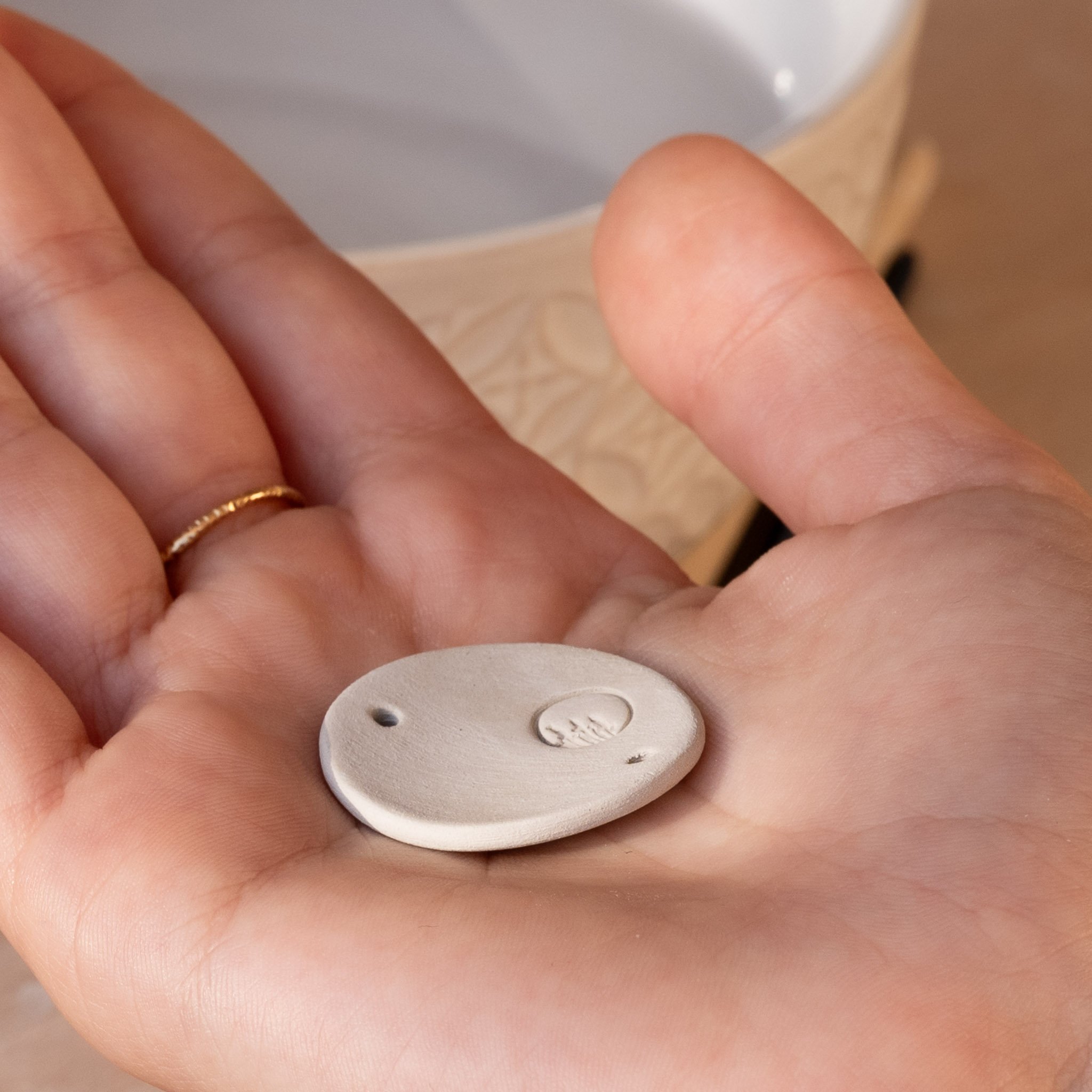 Main ouverte présentant l'envers d'un médaillon en céramique tout juste cuit, dévoilant notre poinçon d'artisan, symbole de notre engagement.