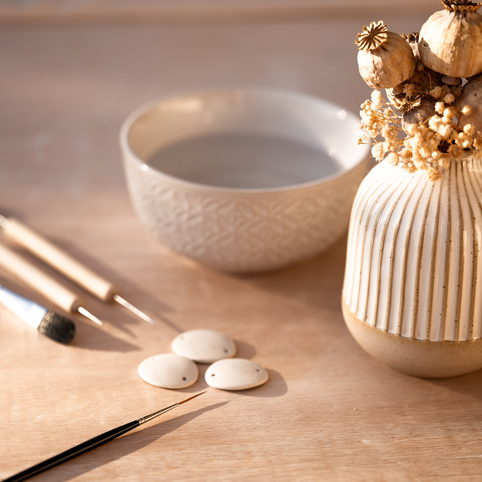 Ébauches de bijoux en argile avant cuisson et outils d'artisan, témoignant du travail manuel et du savoir-faire unique de nos créations.