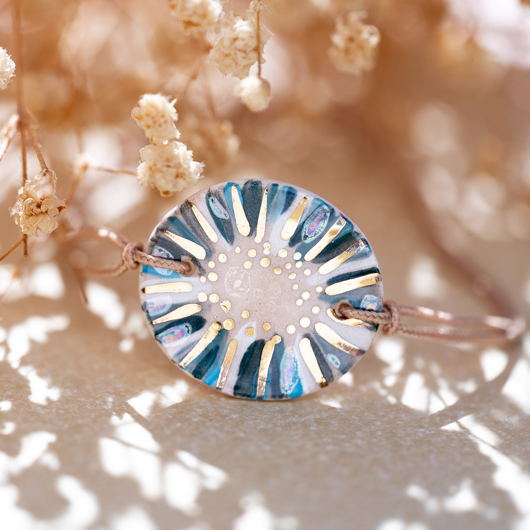 Bracelet en céramique Cala Gioia aux nuances bleues et éclats d'or fin, posé dans une lumière chaleureuse rappelant les reflets du soleil sur la Méditerranée.