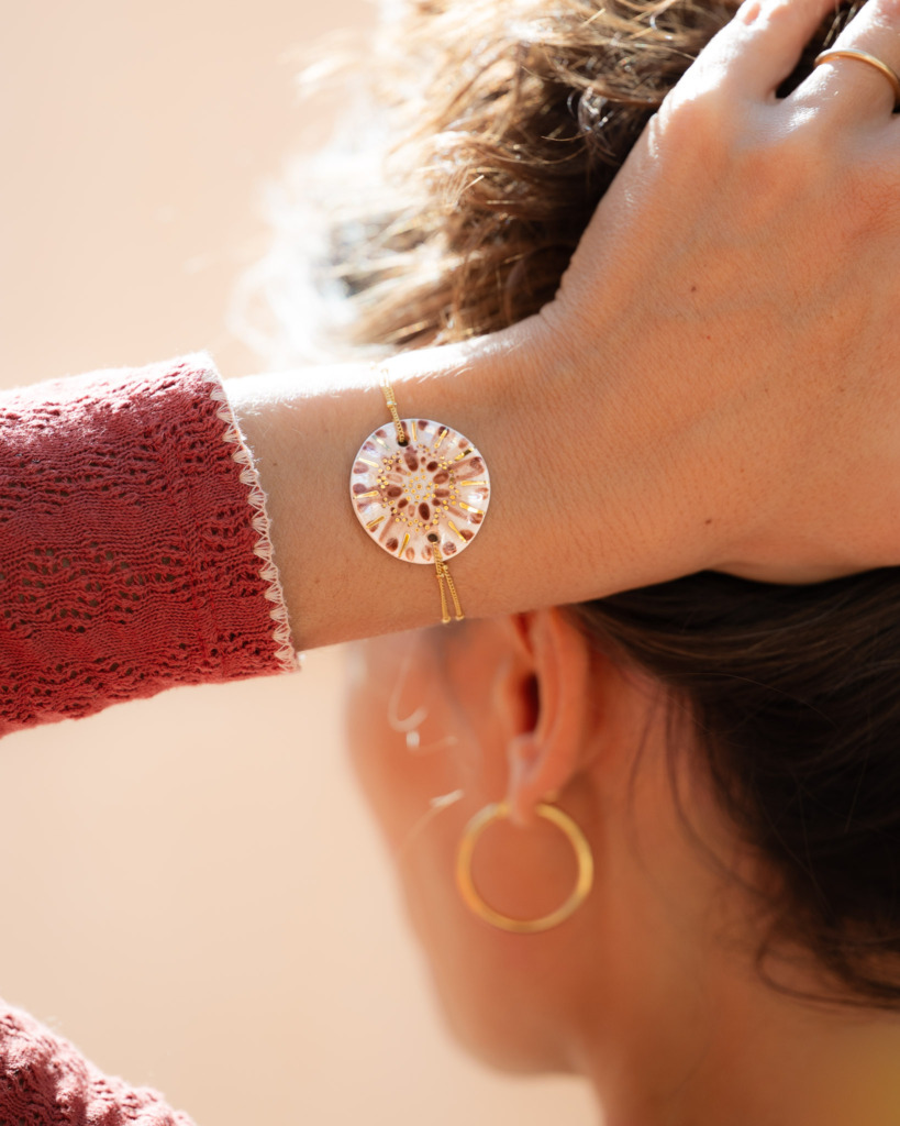 Bracelet Corolle Ambrée sur chaîne perlée or laminé, porté au poignet d'une main glissée dans les cheveux - Cala Gioia