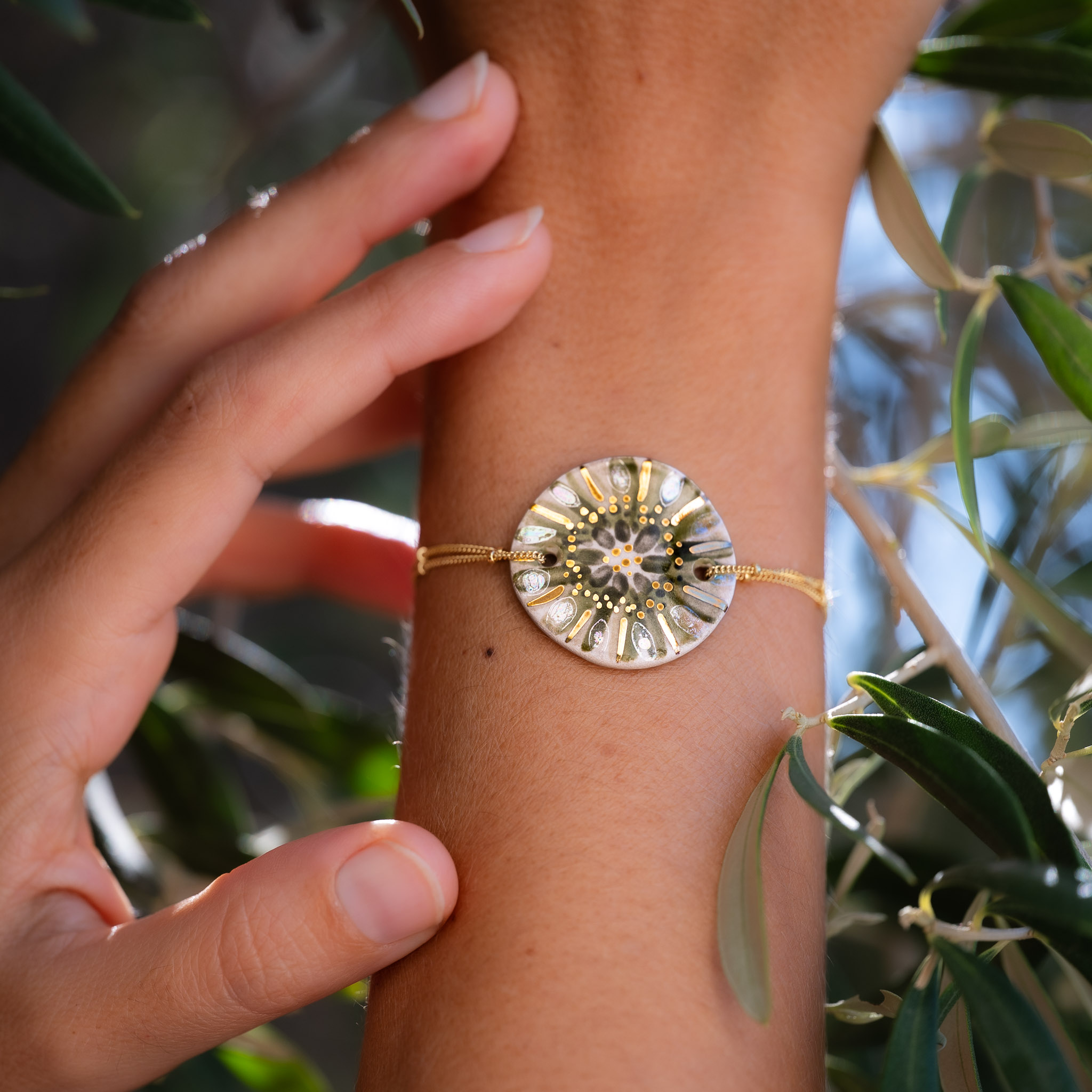 Bracelet Feuillage Irisé sur chaîne perlée en or laminé porté au poignet, parmi les feuilles d'olivier - Cala Gioia